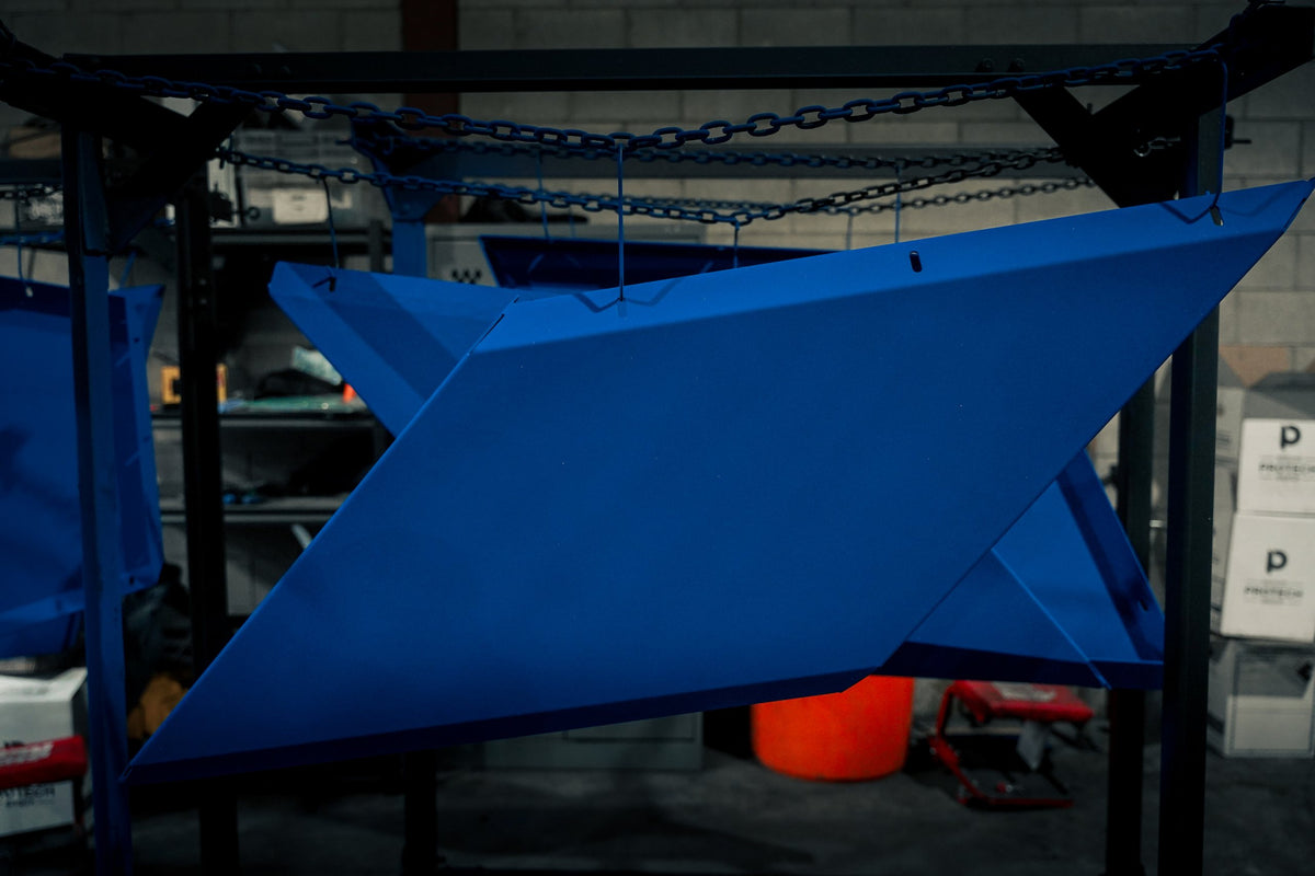 Steel panel powder coated in blue hanging from a mobile rack in the shop
