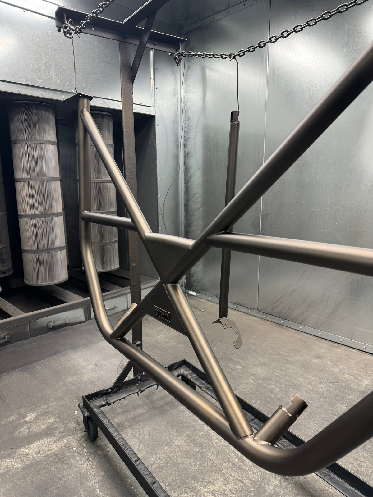 Tube frame powder coated in bronze on a rack in the booth