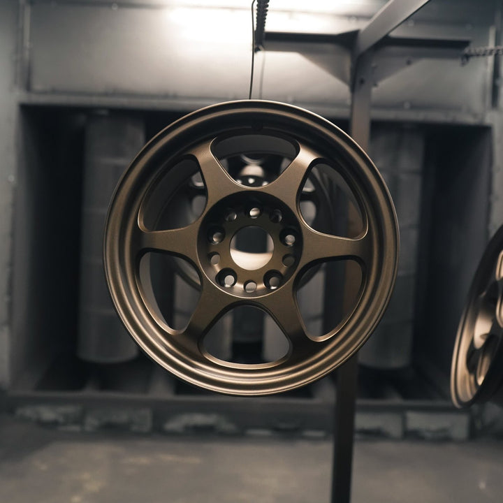 Front view of a six-spoke wheel powder coated in matte bronze in the booth