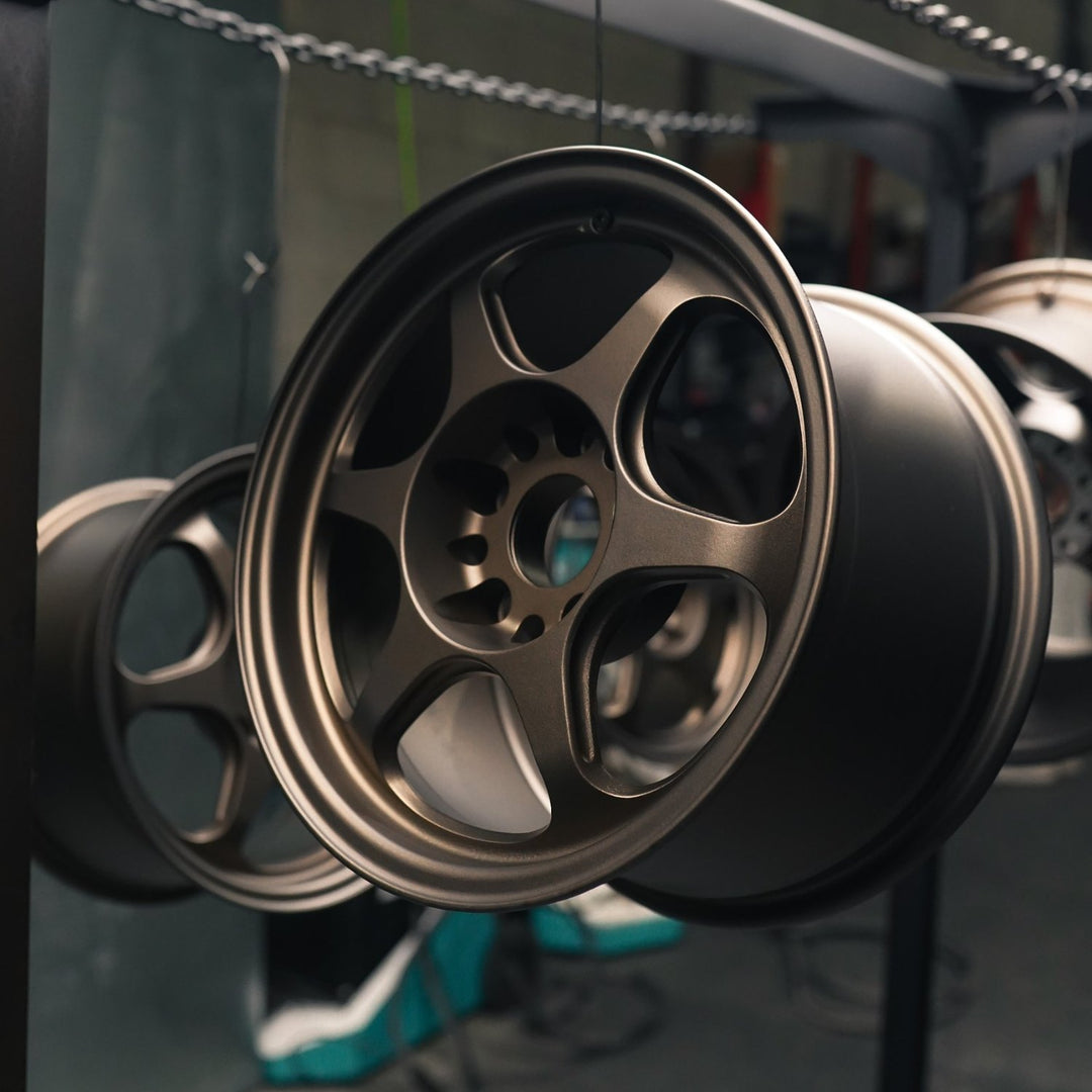 Six-spoke wheel powder coated in matte bronze hanging on a rack