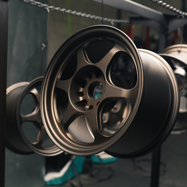 Six-spoke wheel powder coated in matte bronze hanging on a rack