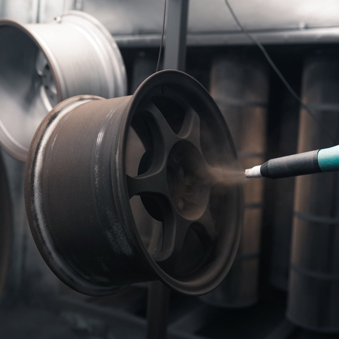 Electrostatic gun applying bronze powder to a wheel