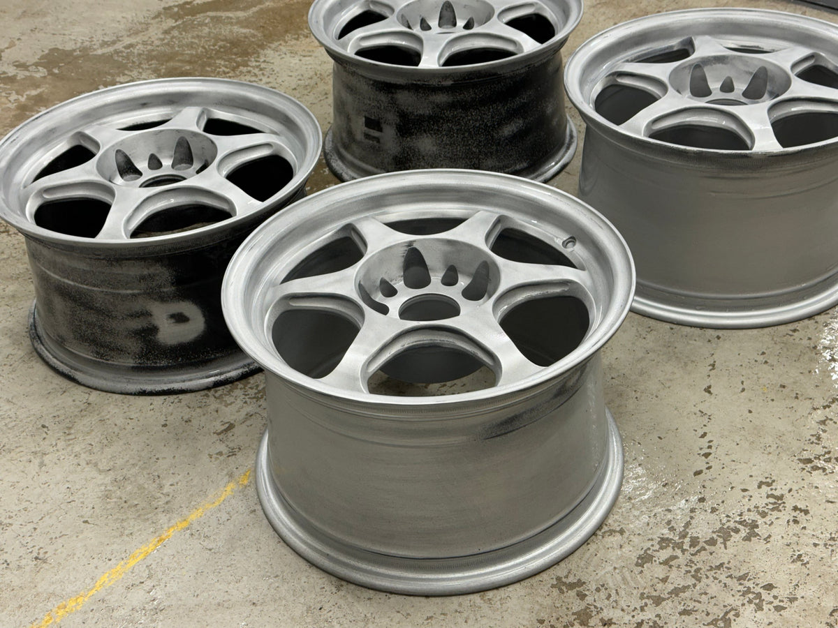 Four aluminum wheels blasted to bare metal on the floor before powder coating