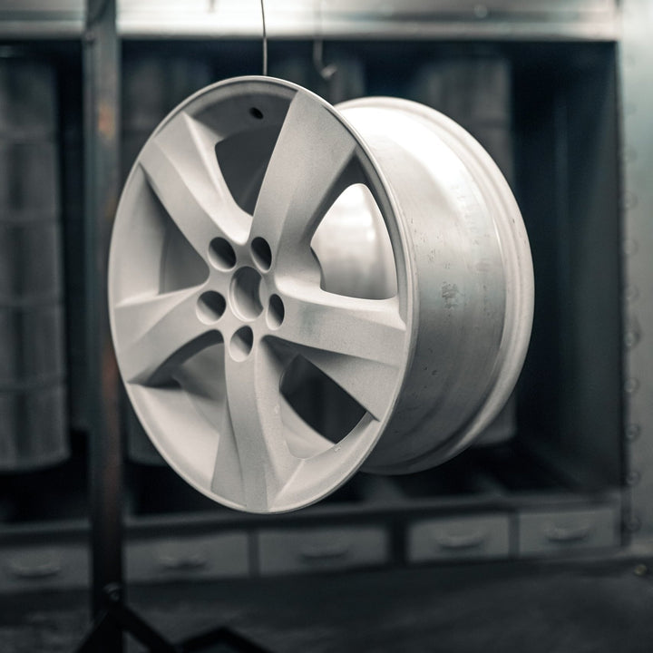 Bare aluminum wheel hanging in the booth before powder coating