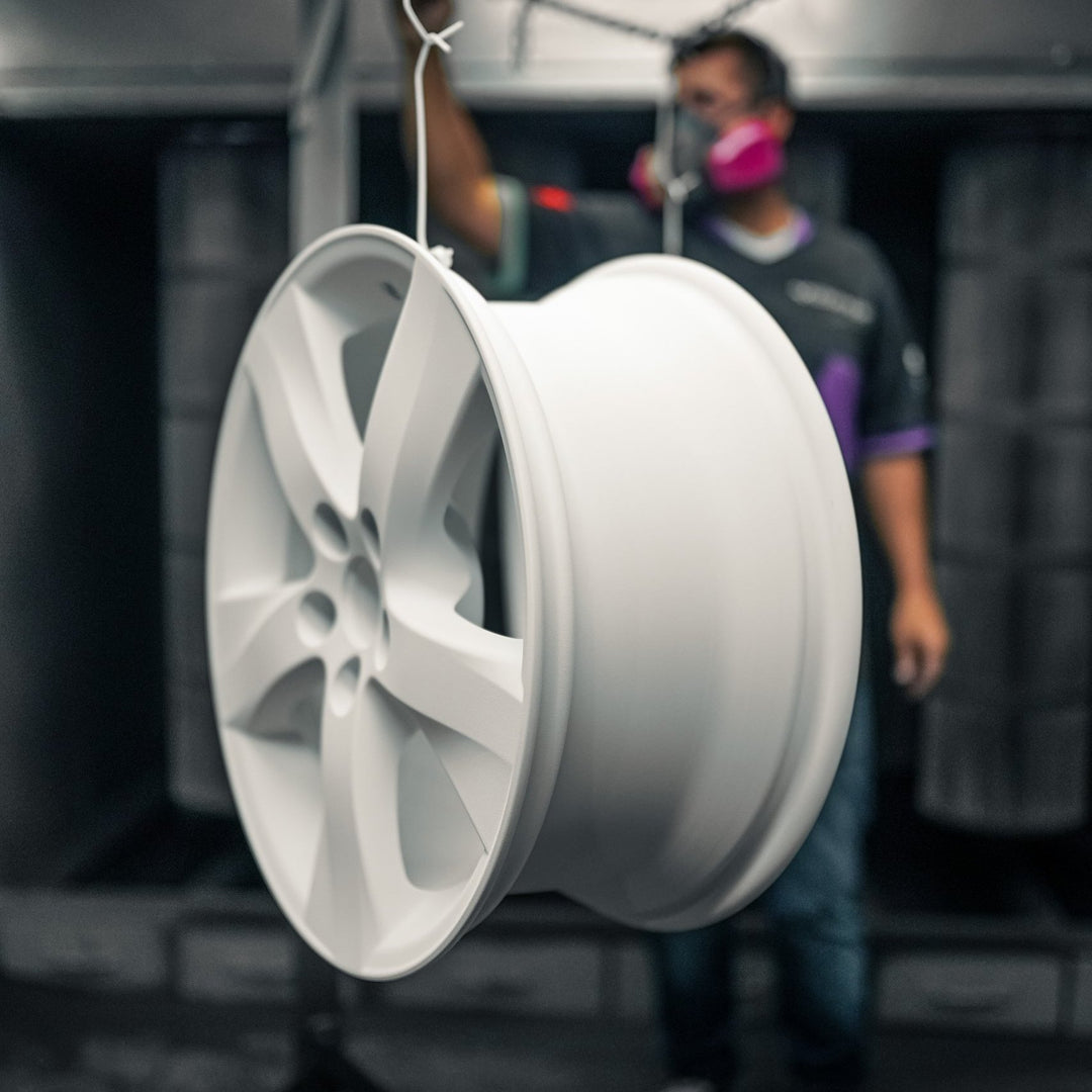 Bare aluminum wheel hanging in the booth, painter in the background