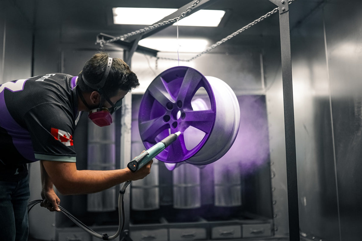 Peintre qui applique de la poudre violette sur une jante au pistolet électrostatique, en cabine