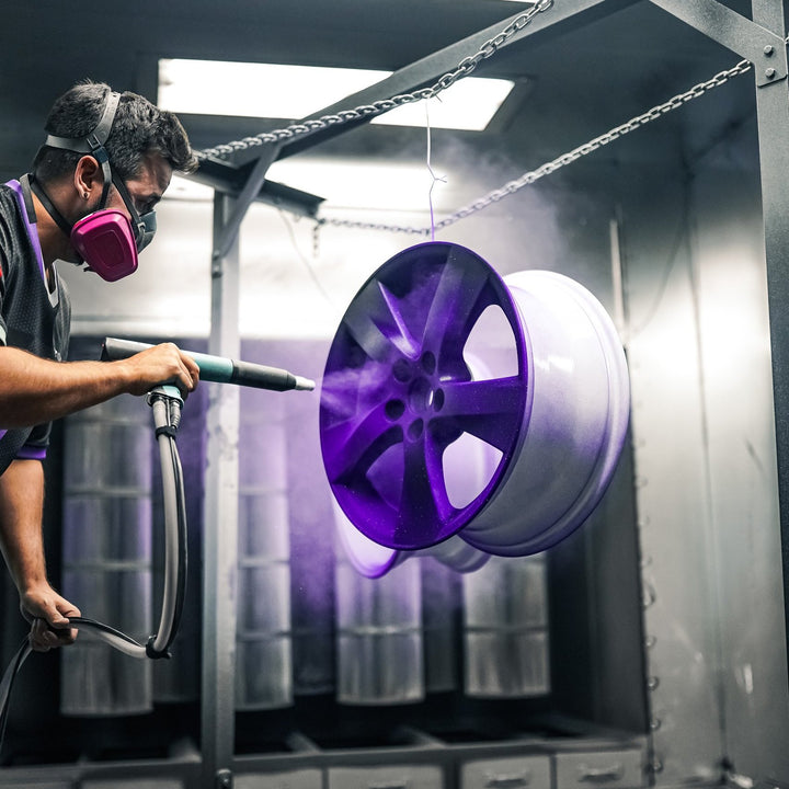 Painter applying purple powder to a wheel with an electrostatic gun