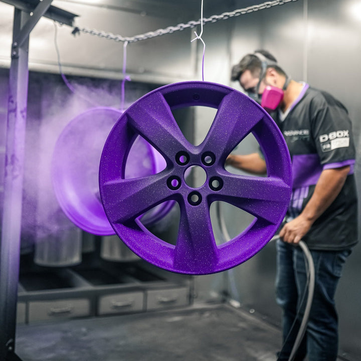 Painter applying a coat of purple powder to a wheel in the booth