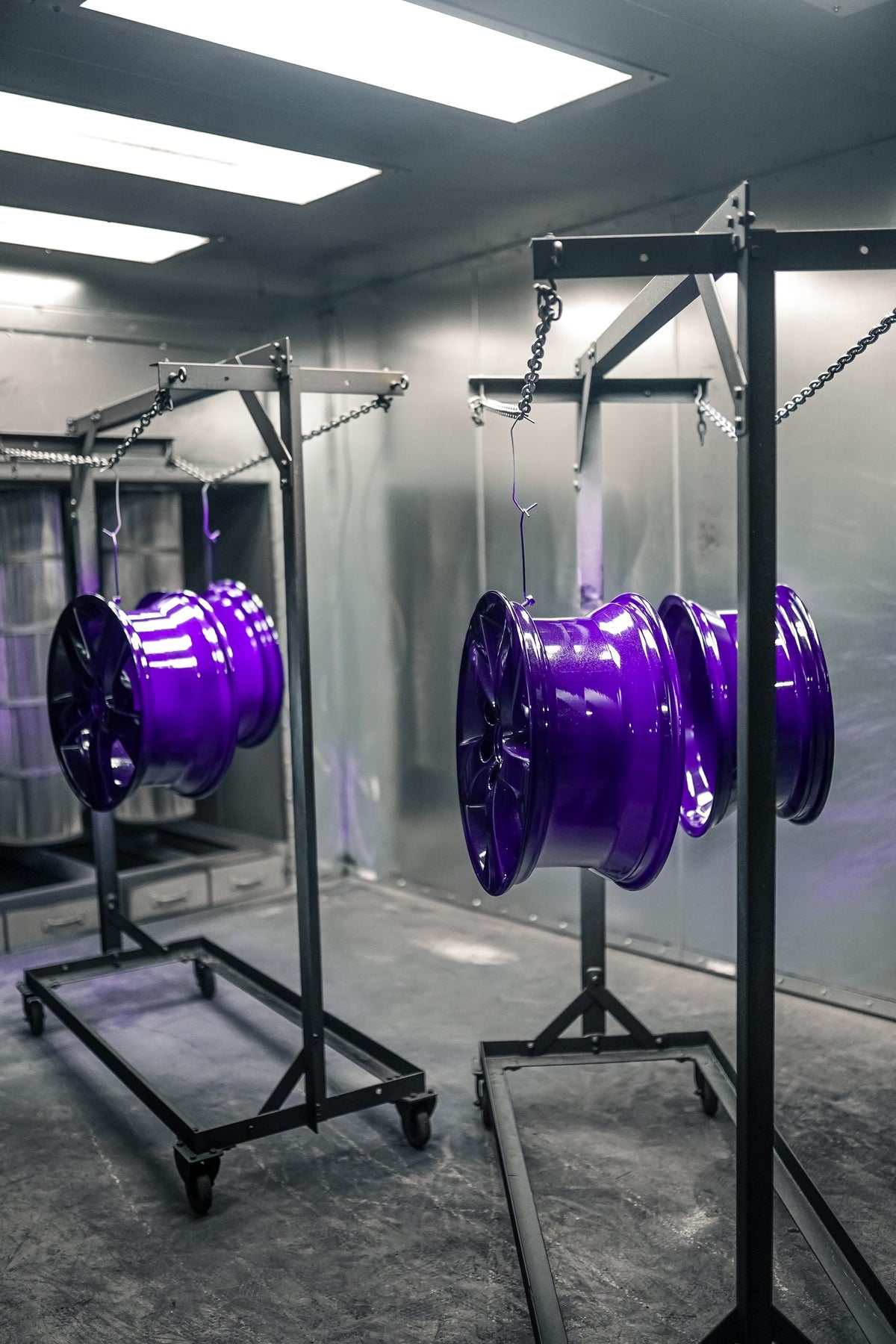 Jantes peintes en poudre violet lustré sur des supports à roulettes dans la cabine