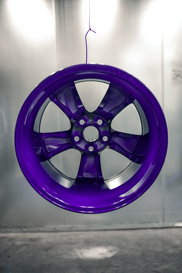 Wheel powder coated in gloss purple hanging against the booth wall